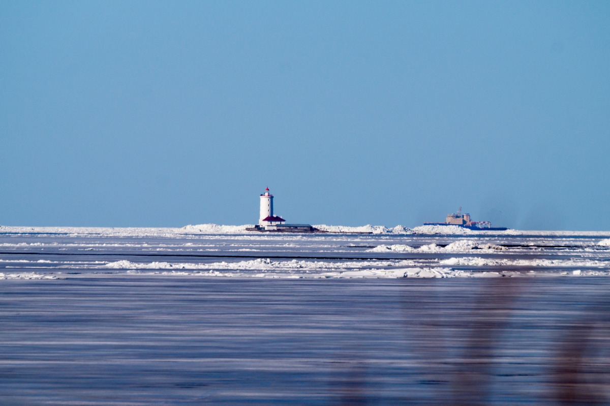 Западный Котлин. На песчаном пляже а конце марта. Вид на маяк и маленький кораблик.